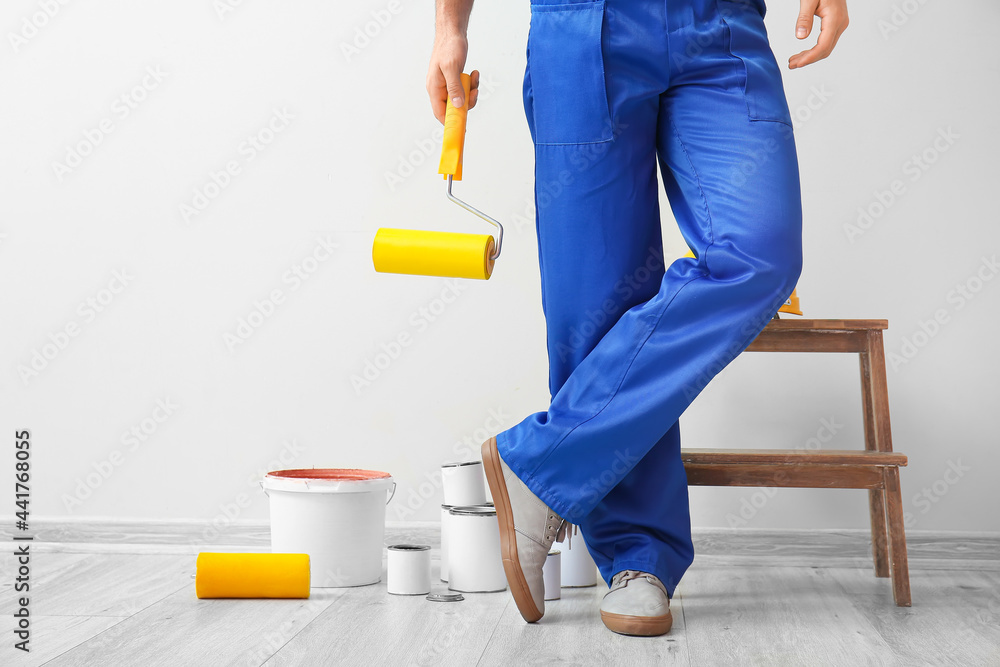 Man with roller and cans of paint near light wall