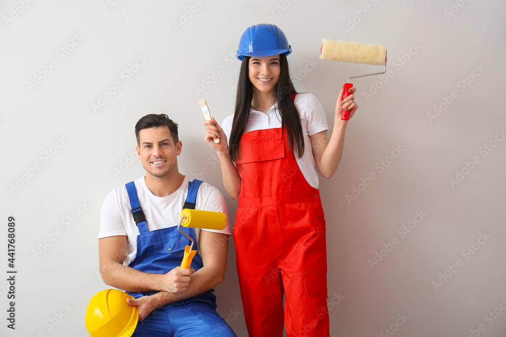 Young couple with rollers and brush on light background