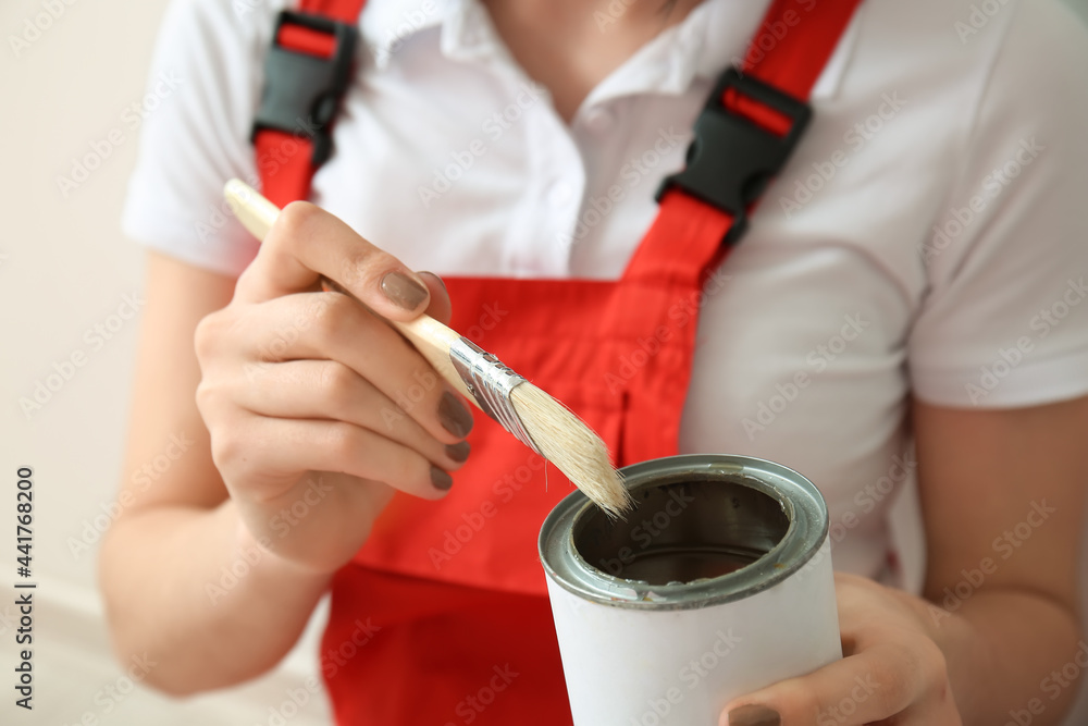 Young woman with brush and can of paint on light background, closeup