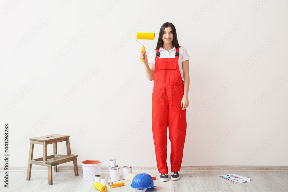 Young woman with paint rollers and cans of paint near light wall