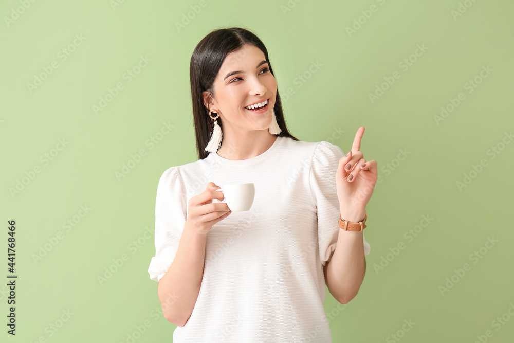 Beautiful young woman with cup of coffee pointing at something on color background