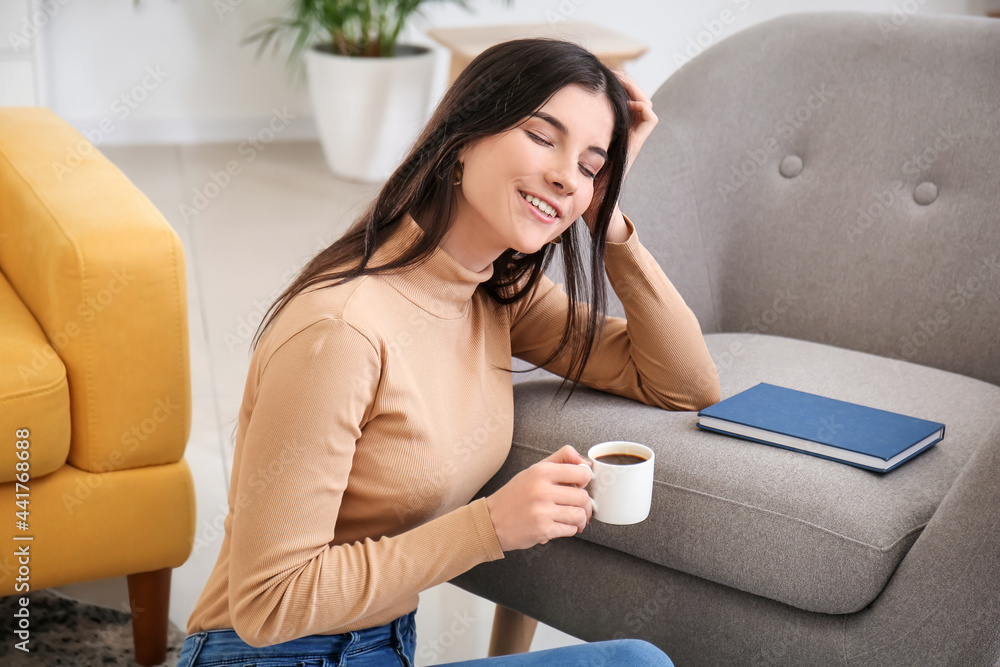 Beautiful young woman with book drinking coffee at home