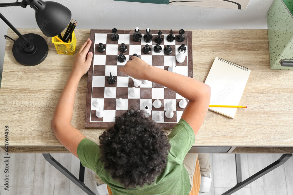 Cute African-American boy playing chess at home, top view