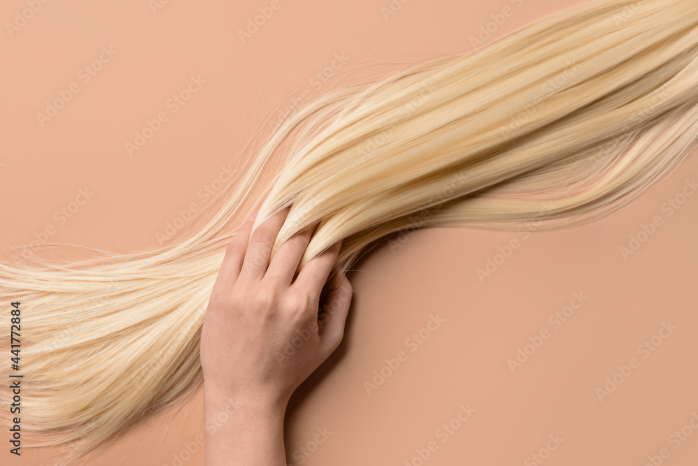 Woman with strand of blonde hair on color background