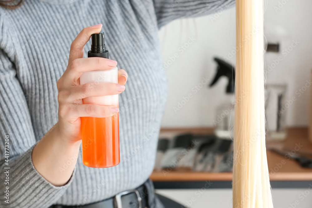 Female hairdresser spraying strand of blonde hair in beauty salon, closeup