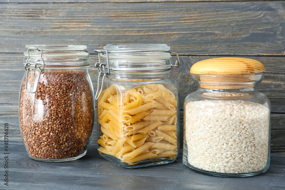 Glass jars with different products on dark wooden background