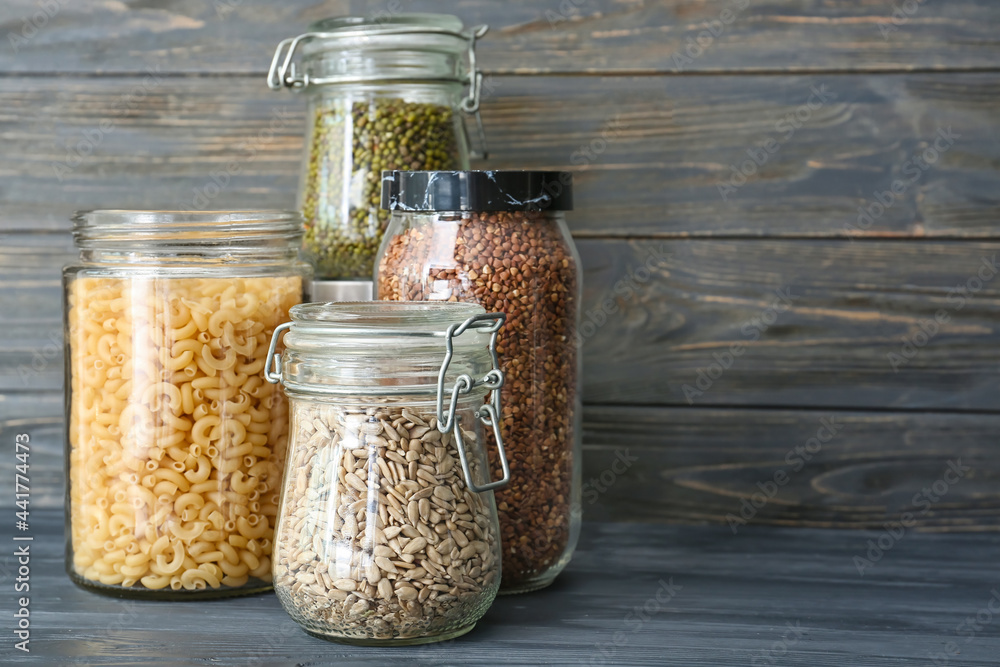 Glass jars with different products on dark wooden background