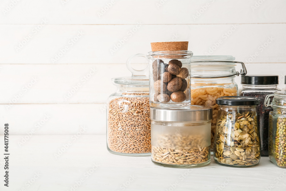 Glass jars with different products on light wooden background