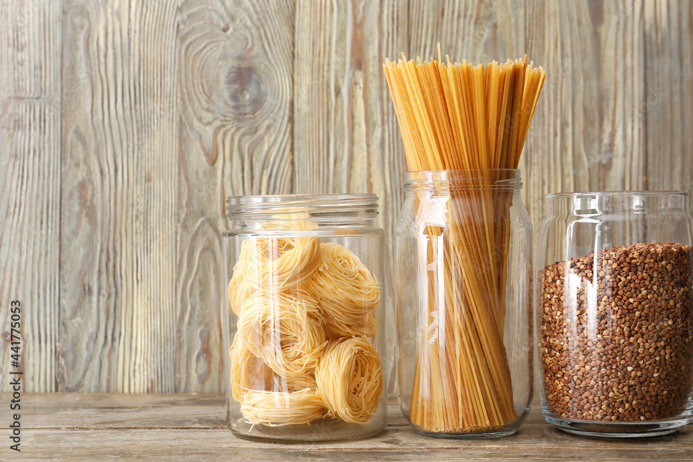 Glass jars with buckwheat and pasta on wooden background