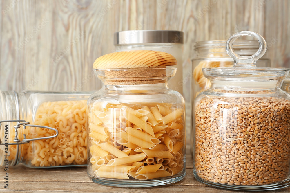 Glass jars with raw pasta and wheat grains on wooden background