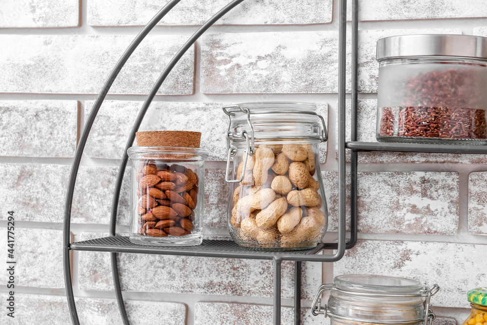 Jars with different products on shelf near brick wall