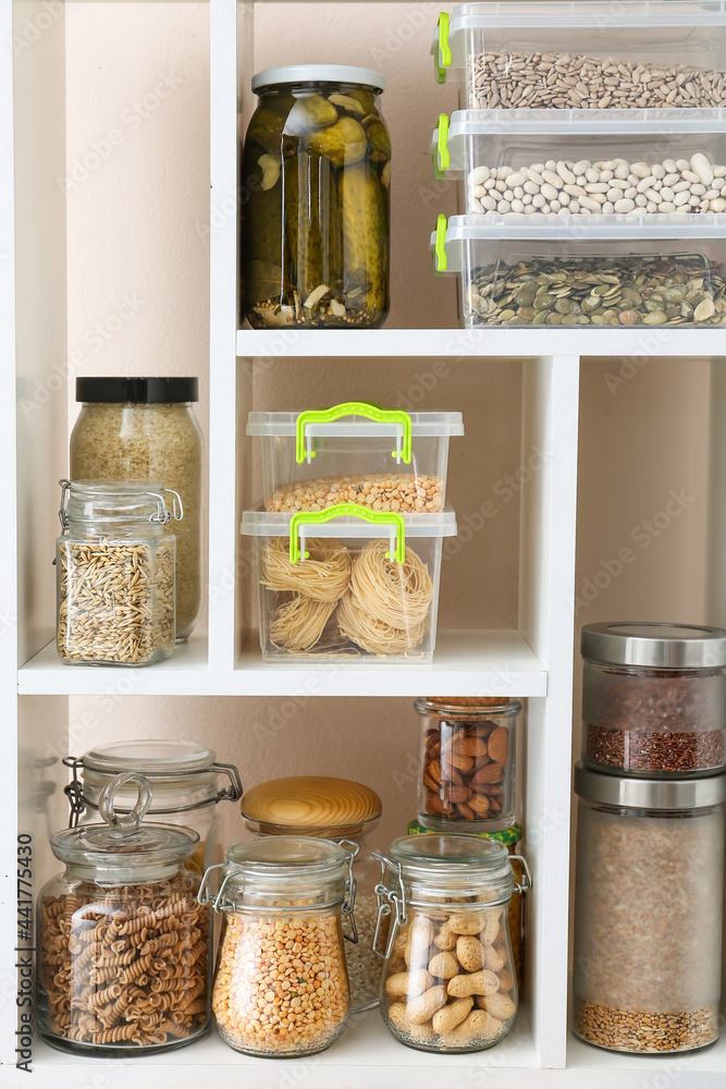 Jars and containers with different products on shelves near color wall