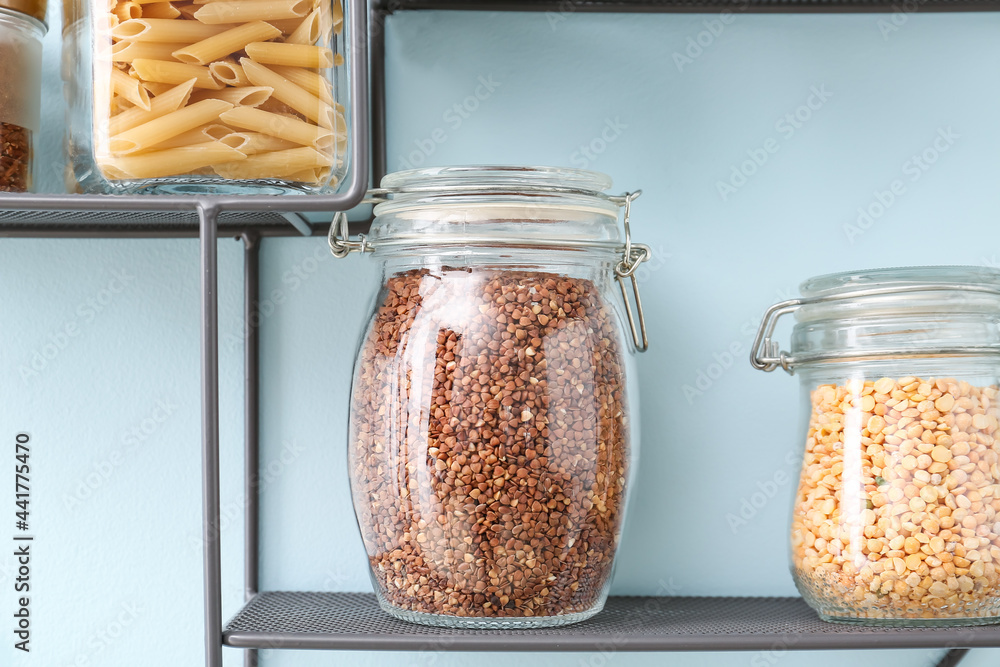 Jars with different products on shelf near color wall