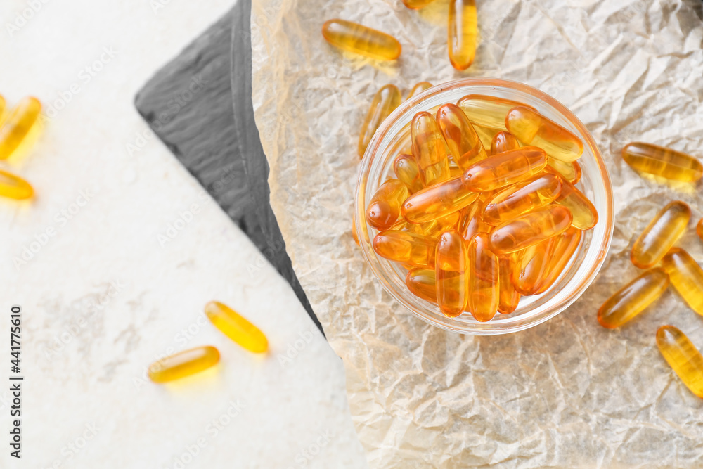 Bowl with fish oil pills on light background