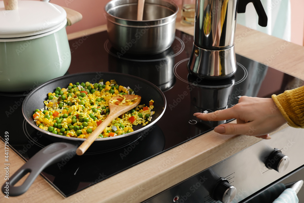 Woman cooking tasty rice with vegetables on stove in kitchen, closeup