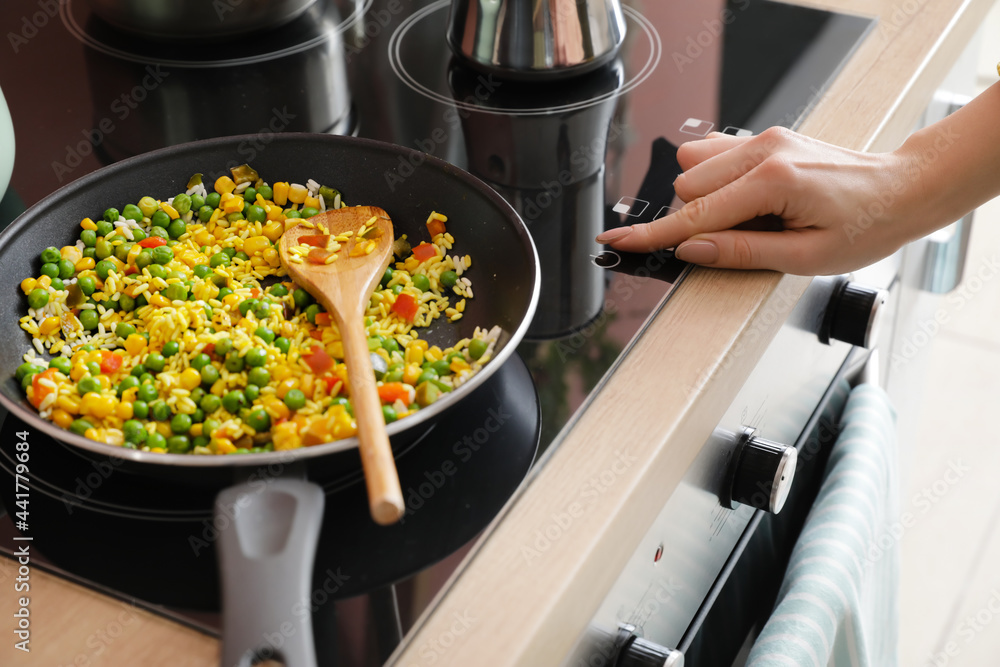 Woman cooking tasty rice with vegetables on stove in kitchen, closeup