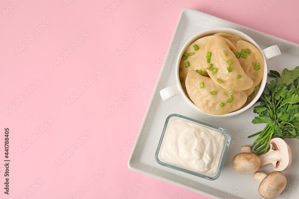 Plate with tasty dumplings, sour cream and fresh ingredients on color background