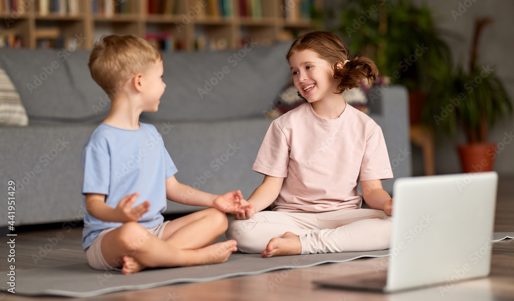 Two happy kids sitting in lotus pose and smiling while practicing yoga online