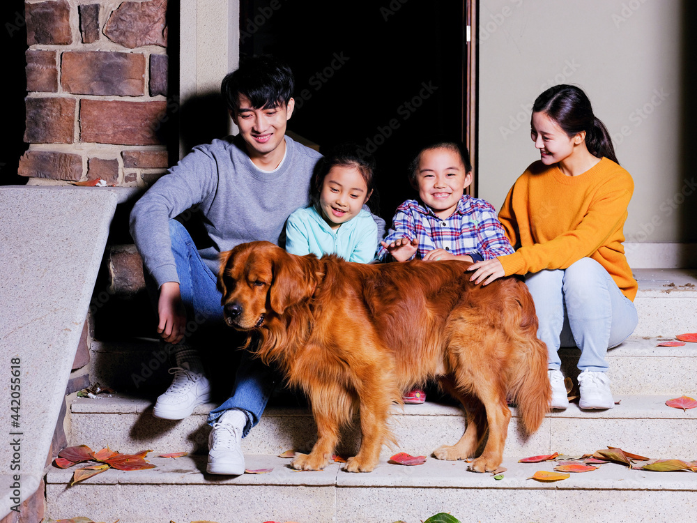 A happy family of four sitting on the steps with their pet dog