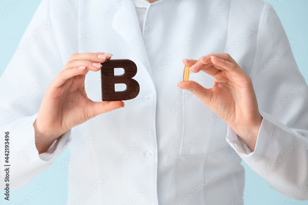 Female doctor holding letter B and pill on color background, closeup