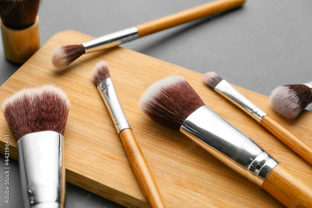 Board with set of makeup brushes on dark background