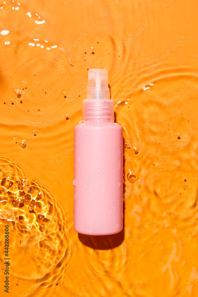 Bottle of cosmetic product in water on color background