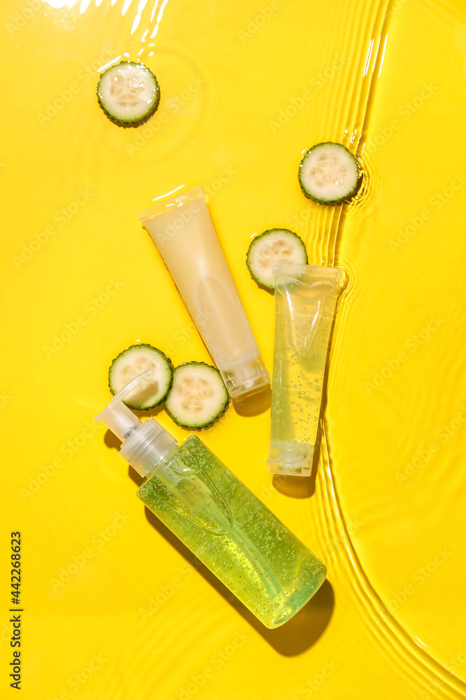 Different cosmetic products and slices of cucumber in water on color background