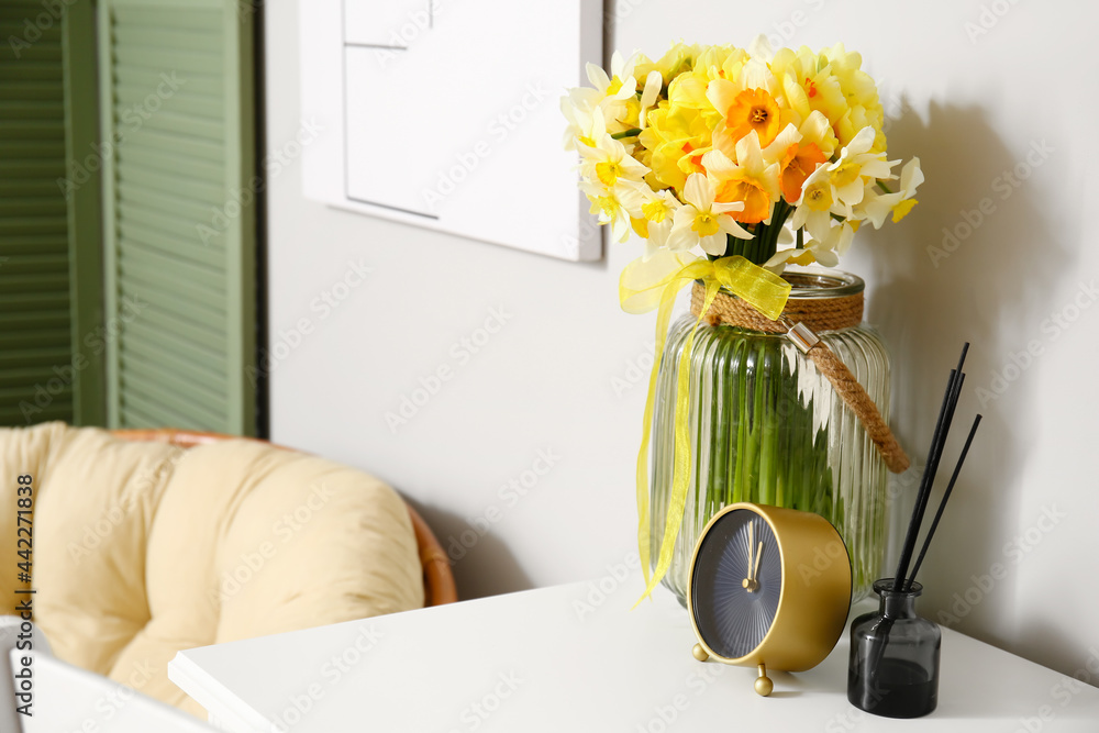 Vase with beautiful narcissus flowers on table in room