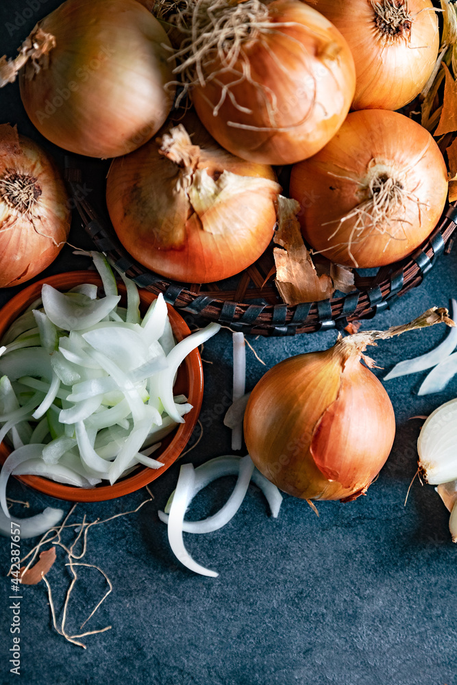 Cebollas y rodajas sobre tabla de cortar de madera y cesto de mimbre. Fondo de alimentos saludables.