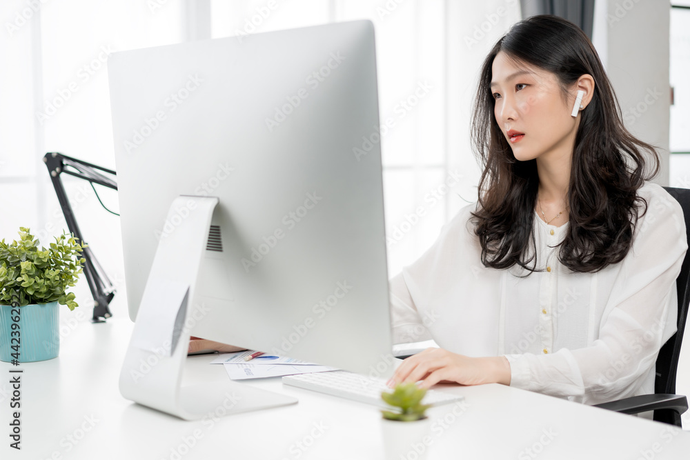 Young asian girl working at a home with a computer and wearing earphones