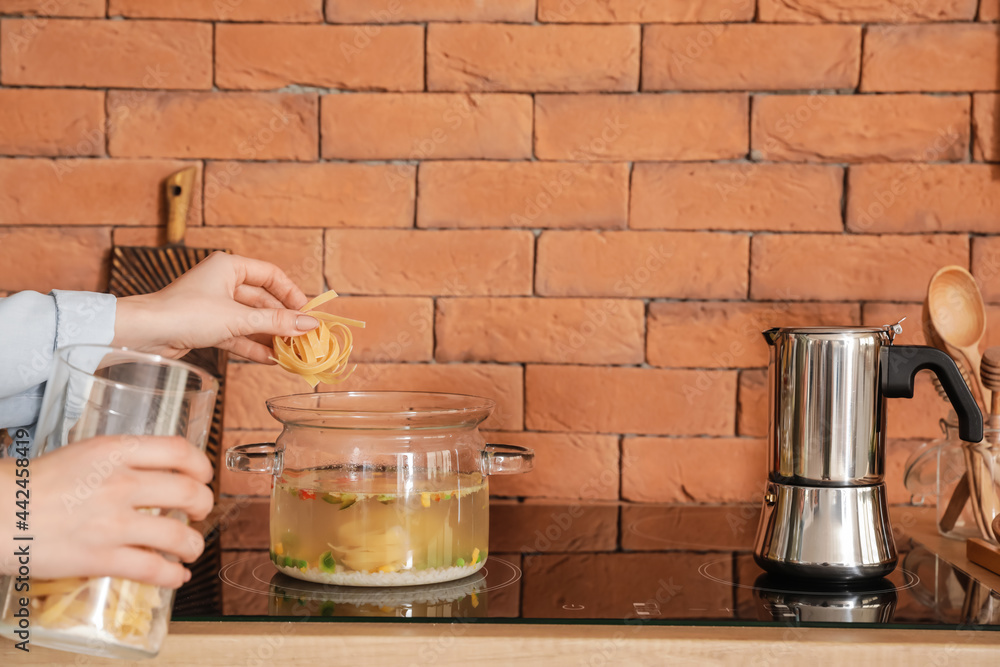 Woman cooking tasty soup on stove in kitchen