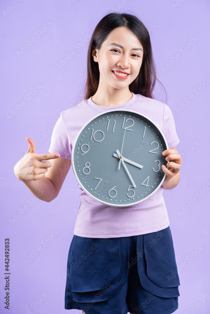 Young Asian woman holding a watch on purple background