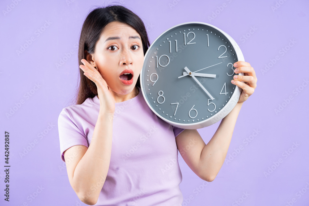 Young Asian woman holding a watch on purple background