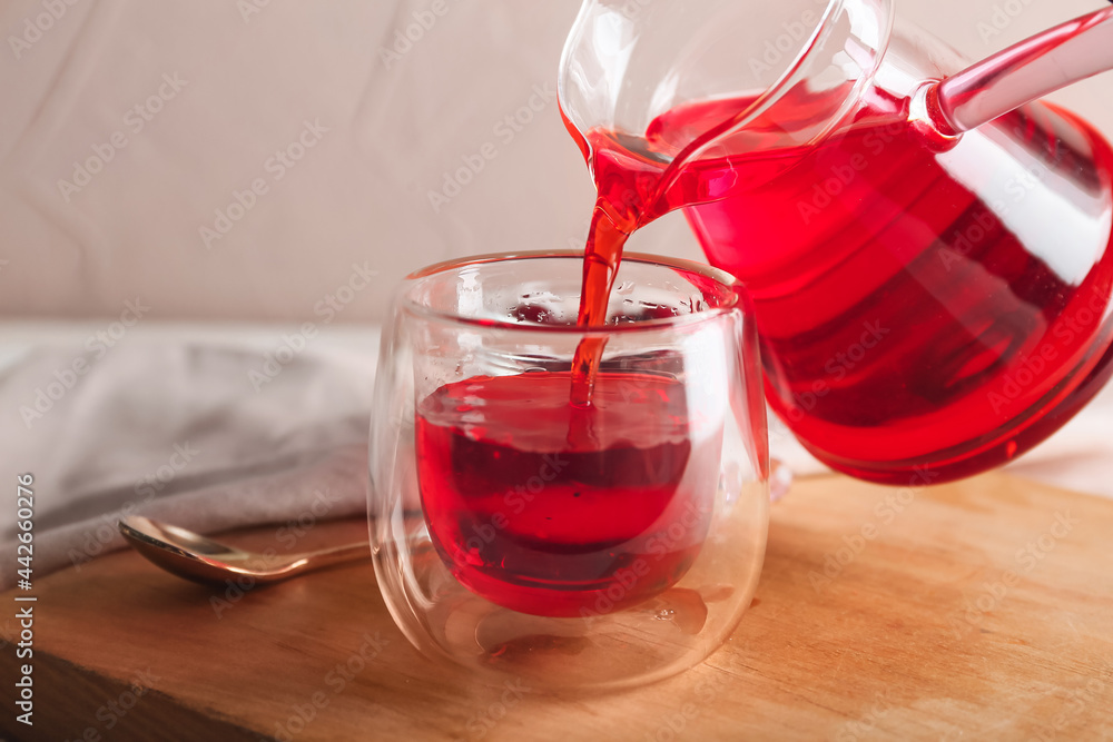 Pouring of hot red tea in glass on table