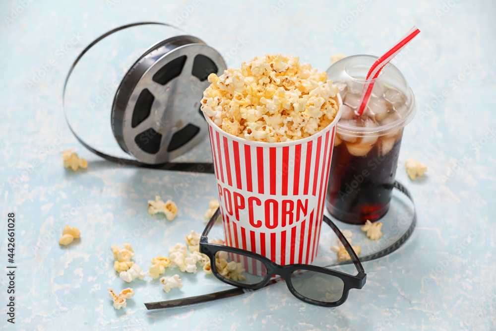 Tasty popcorn with 3D glasses, cola and film reel on color background