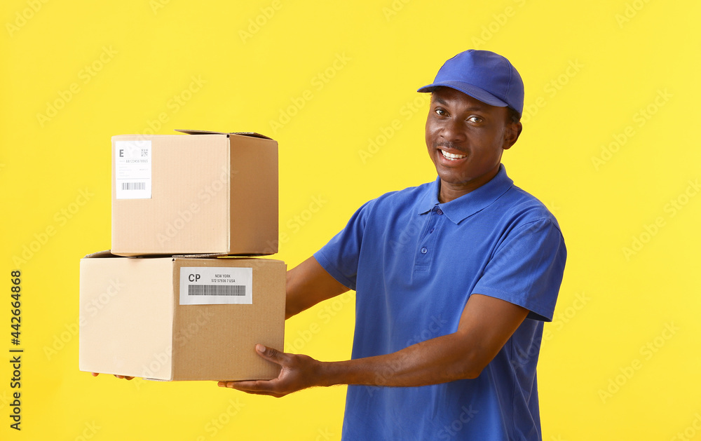 African-American delivery man with parcels on color background