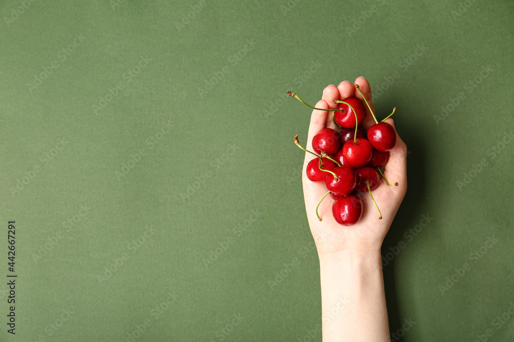 Female hand with heap of tasty ripe cherry on color background