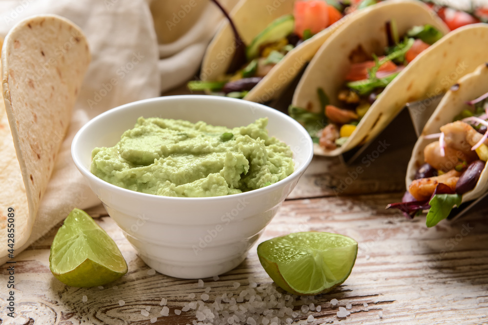 Tacos and tasty guacamole in bowl on light wooden background, closeup