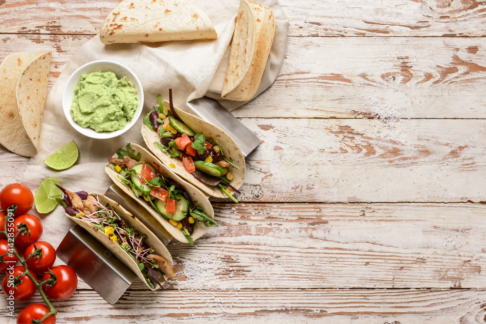 Composition with tacos and tasty guacamole in bowl on light wooden background