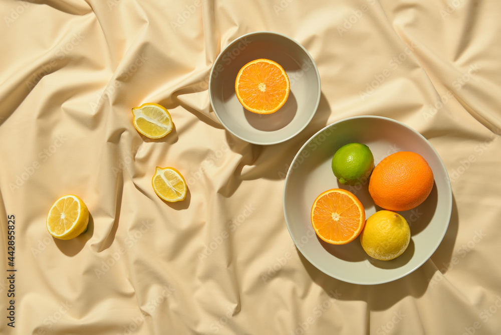 Bowls with healthy citrus fruits on light fabric background