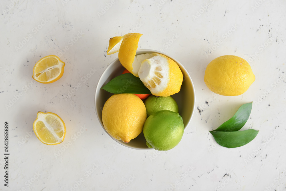 Bowl with healthy citrus fruits on light background