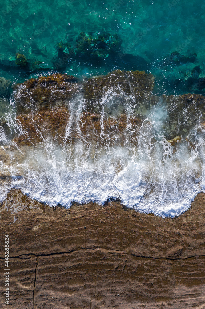 海浪在棕色悬崖岩石上破碎，潮水不断上涨，无人机正上方视角