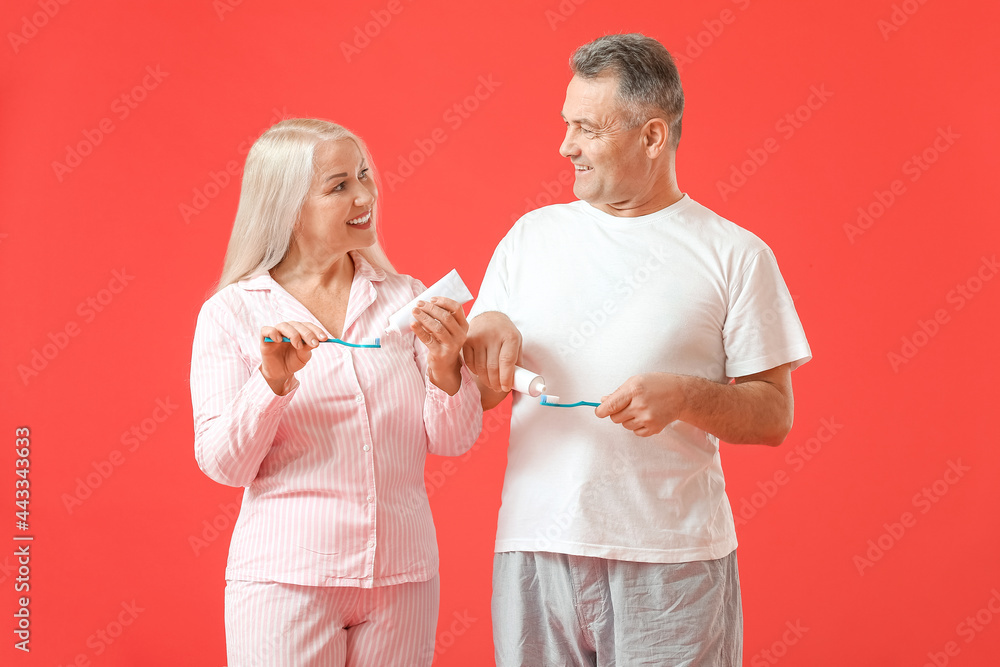 Mature couple brushing teeth on color background