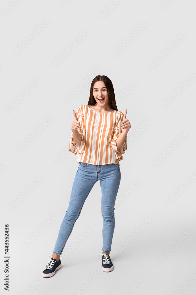 Beautiful young woman showing thumbs-up on light background