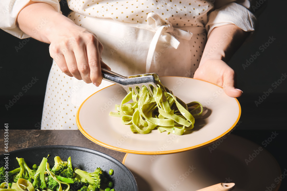 女人把美味的意大利面和蔬菜从煎锅里放进餐桌上的盘子里