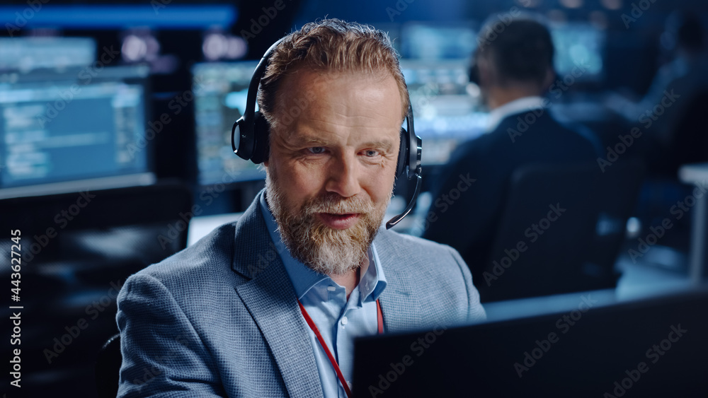 Bearded Happy Senior Technical Support Specialist is Talking on a Headset while Working on a Compute