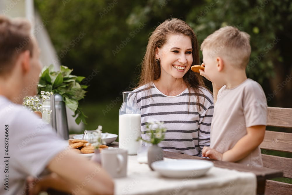 家庭午餐：夏天在花园里，爸爸妈妈和孩子笑着吃带牛奶的饼干