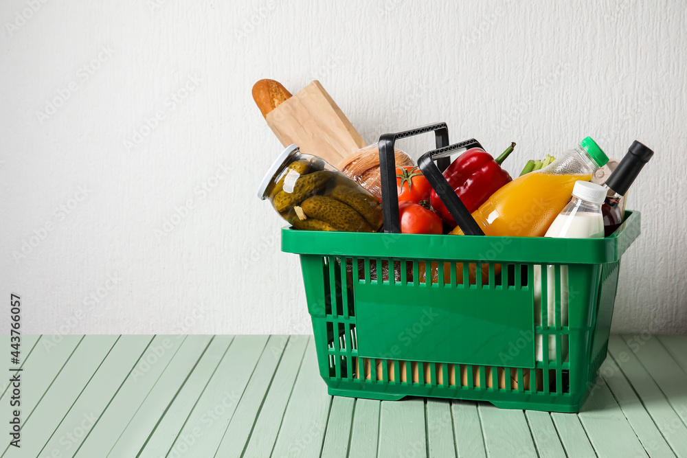 Shopping basket with food on table near white wall