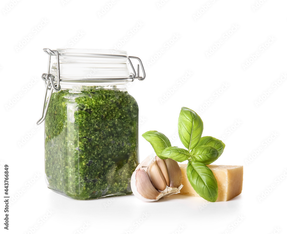 Jar with fresh pesto sauce and ingredients on white background