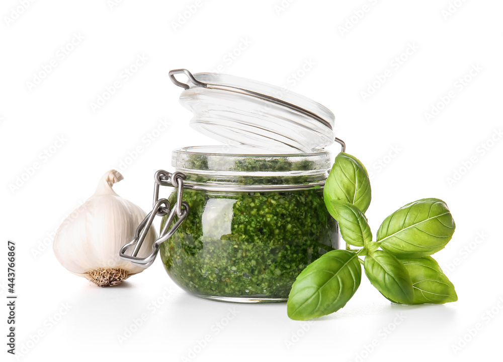 Jar with fresh pesto sauce, basil leaves and garlic on white background